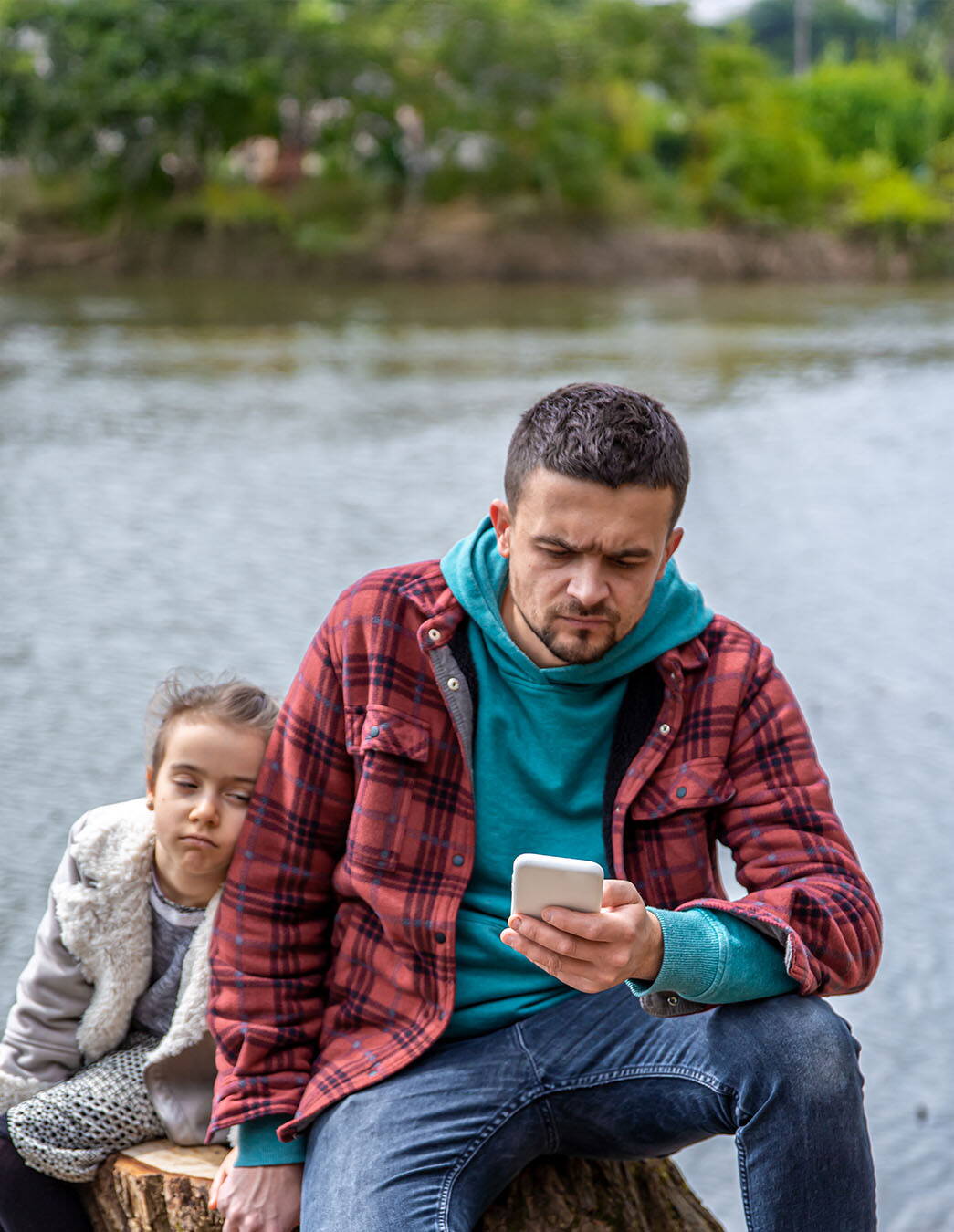 Une personne regarde son smartphone tandis qu’un enfant est assis à côté. Les distractions numériques répétées peuvent amener les enfants à se sentir ignorés ou insuffisamment pris en compte.