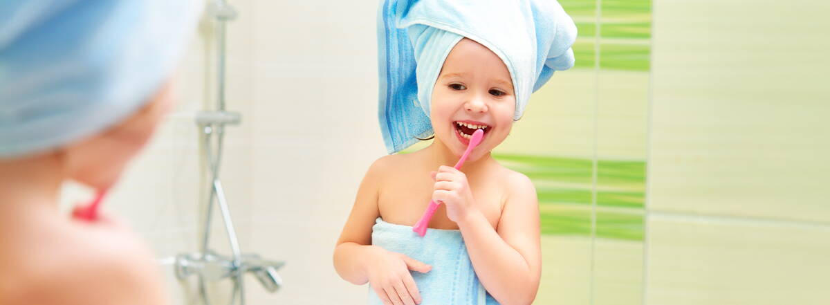 Assicurato con cura dentale Una bambina è davanti allo specchio del bagno e si lava i denti – la migliore protezione inizia con una buona cura e un forte sostegno.