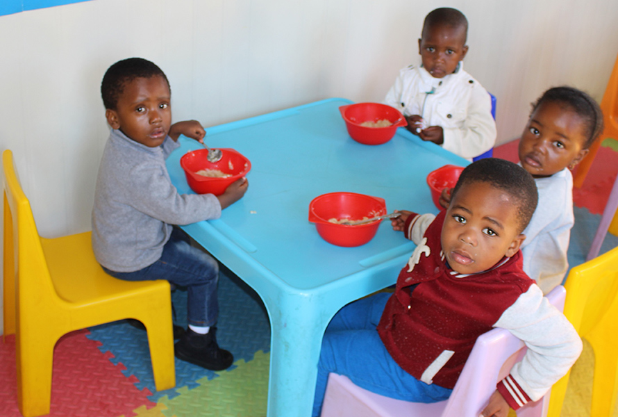Stärkung im Schulalltag Die Kinder der KITA Nkululeko essen gemeinsam am Plastiktisch. Die ausgewogene Ernährung gehört zur täglichen Basis für Lernen und Wachsen.