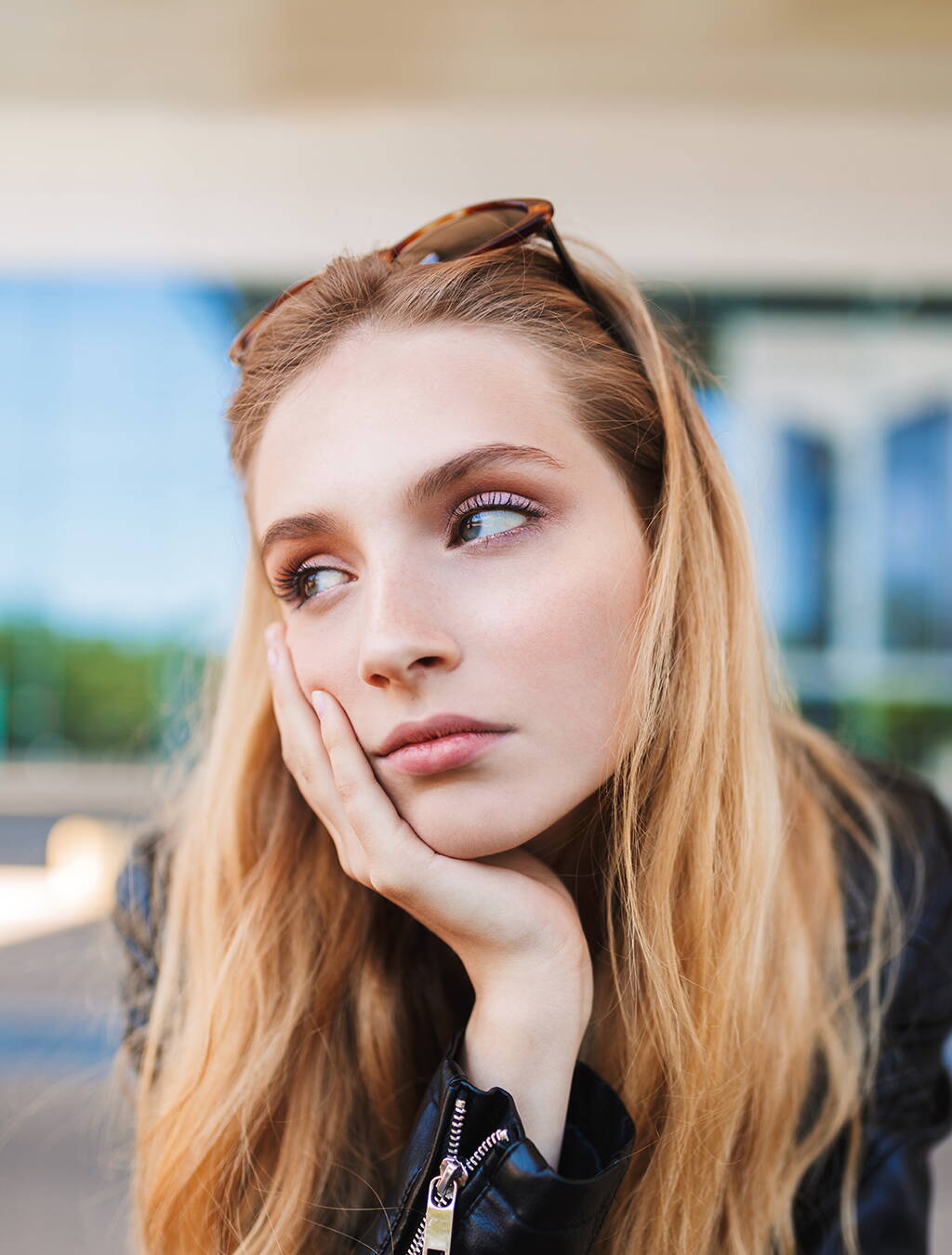 Eine junge Frau stützt nachdenklich den Kopf auf die Hand – die Frage, wann sie die Schwangerschaft verkündet, beschäftigt sie.