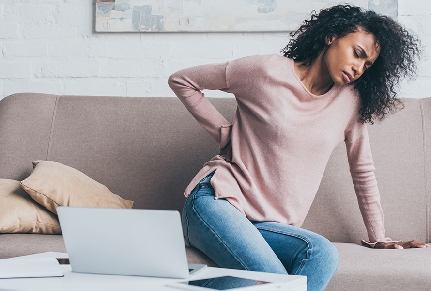 Schwangere mit Rückenschmerzen auf dem Sofa Eine Frau sitzt entspannt auf dem Sofa, hält ihren unteren Rücken – typisches Schwangerschaftssymptom und Tipp für mehr Wohlbefinden.