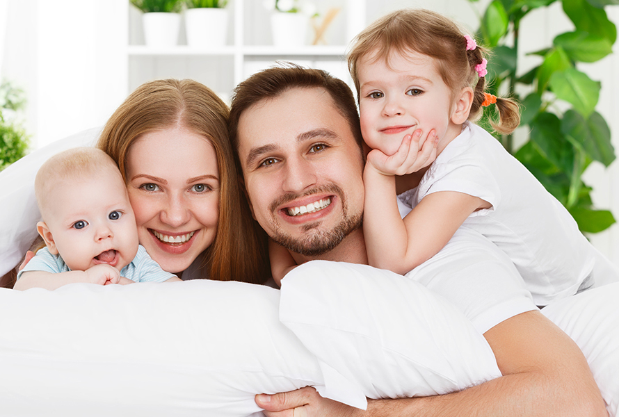 Assicurati in modo adatto alla famiglia Una famiglia allegra guarda direttamente nella fotocamera dal divano – per tutte le vostre domande sulla Soluzione cassa malati.