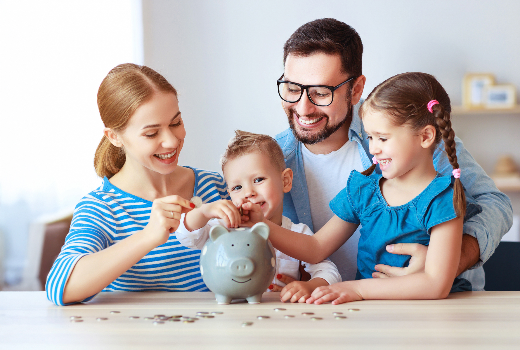 Risparmiare con sistema Una famiglia di quattro persone è seduta al tavolo e riempie un salvadanaio – così gli sconti del contratto collettivo incidono direttamente sul vostro budget familiare.