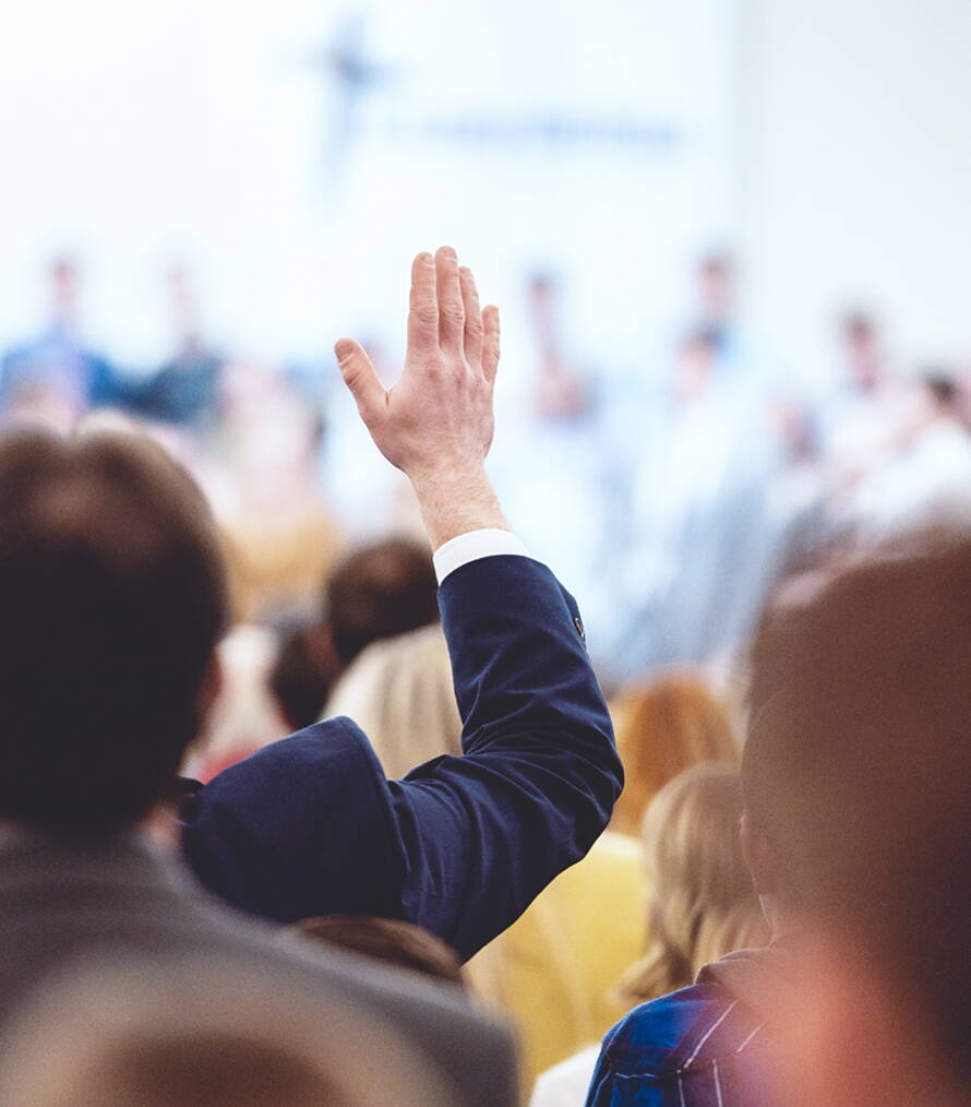 Une participante ou un participant à l’assemblée lève la main pour voter – un moment de démocratie associative vécue.