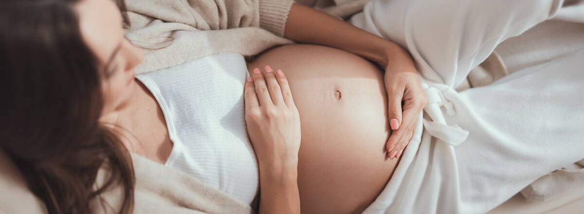 Schwangerschaftskalender Eine schwangere Frau liegt entspannt auf dem Sofa und hält ihren Bauch – ein Moment der Vorfreude, begleitet vom Schwangerschaftskalender.