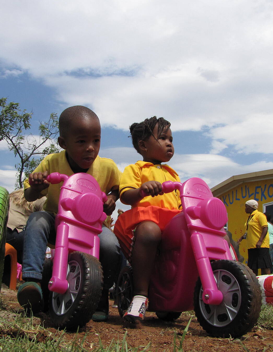 Spielzeit in Nkululeko Ein Junge und ein Mädchen der KITA Nkululeko sitzen lachend auf pinken Plastikmotorrädern – voller Energie und Lebensfreude.