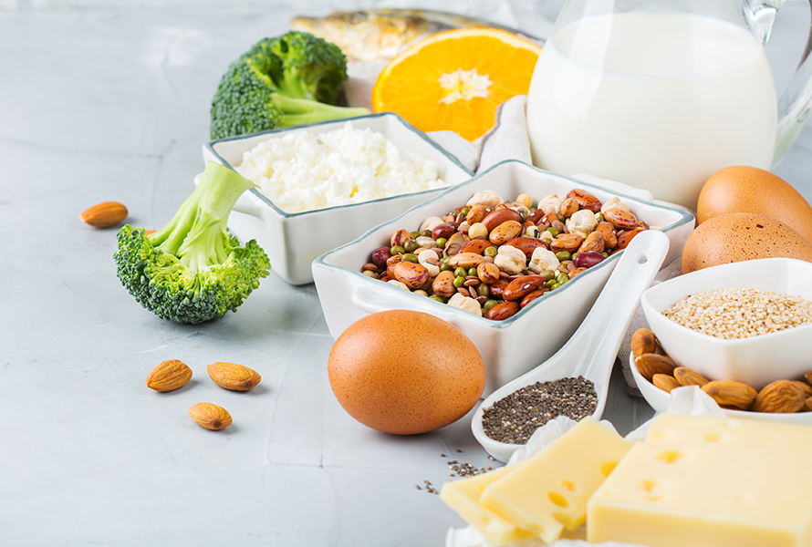 Kalziumhaltige Lebensmittel Eine bunte Auswahl an Hülsenfrüchten, Hüttenkäse, Broccoli, Eiern, Chiasamen, Mandeln und Käse – ideal für den täglichen Kalziumbedarf.