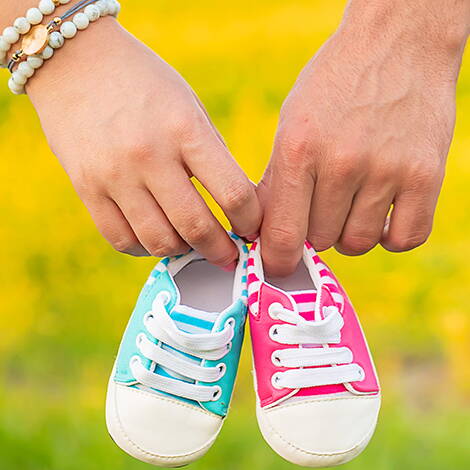 Doppeltes Glück in kleinen Schuhen Zwei Hände halten Babyschuhe in Rosa und Hellblau – ein Symbol für Mehrlingsfreuden und die bevorstehende Geburt.