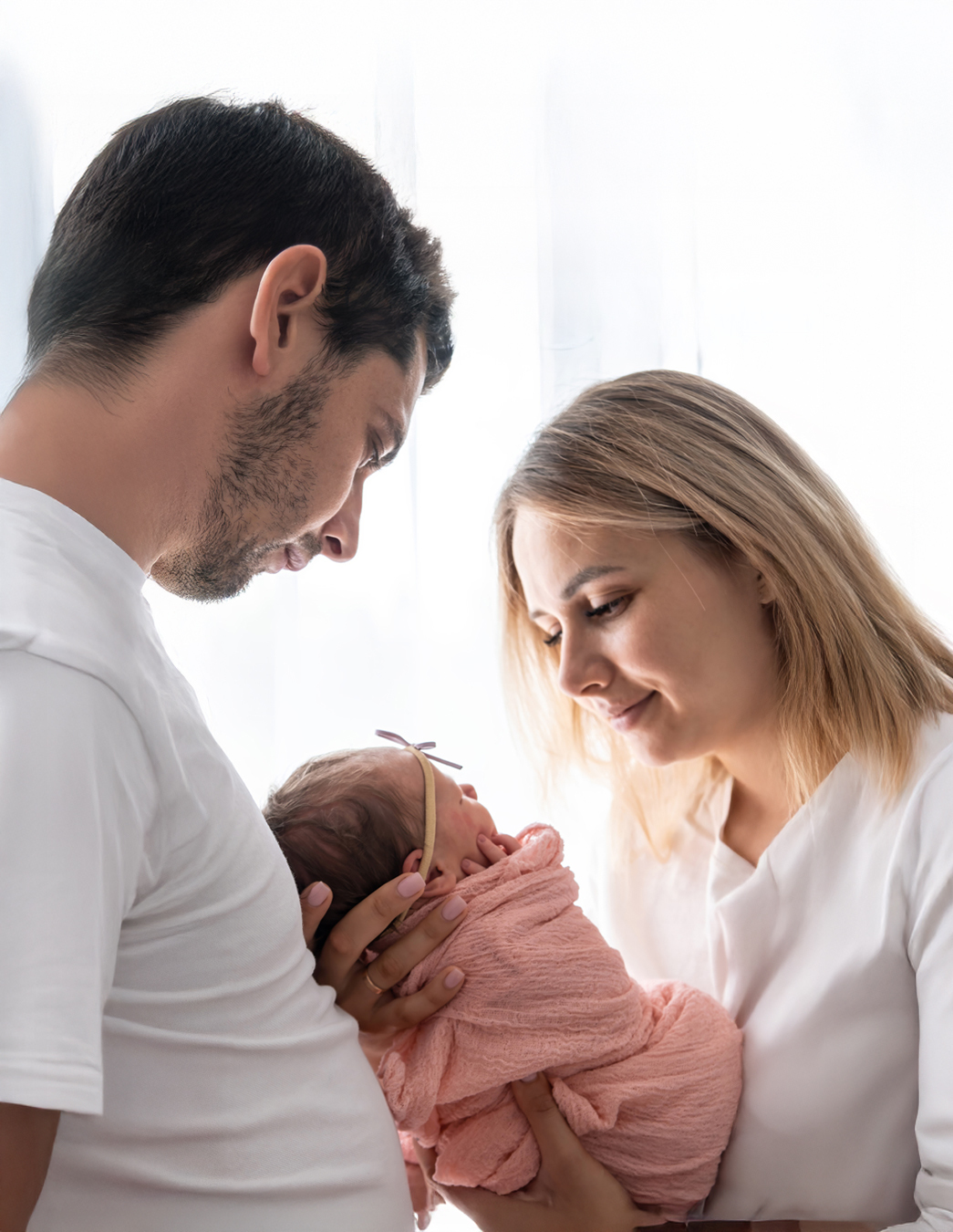 Ein glückliches Paar schaut liebevoll auf das Neugeborene in den Armen der Mutter – ein emotionaler Moment nach einer langen Reise voller Vorfreude und Geduld.
