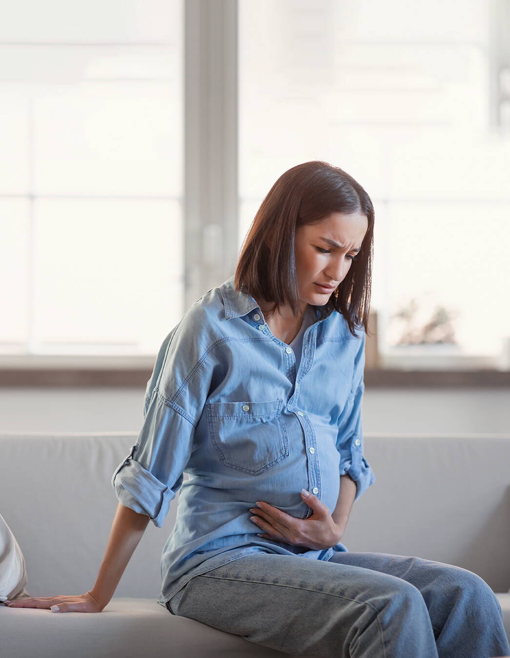 Constipation pendant la grossesse: douleurs abdominales Personne enceinte assise sur un lit tenant son ventre – symptômes fréquents de constipation pendant la grossesse liés aux changements hormonaux et à une digestion ralentie.