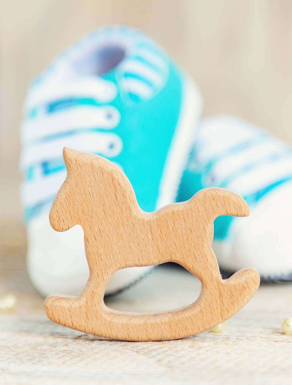 Ein kleines, hölzernes Schaukelpferd im Vordergrund, dahinter zarte hellblaue und weisse Babyschühchen – Sinnbild für die frohe Botschaft in der 13. Schwangerschaftswoche.