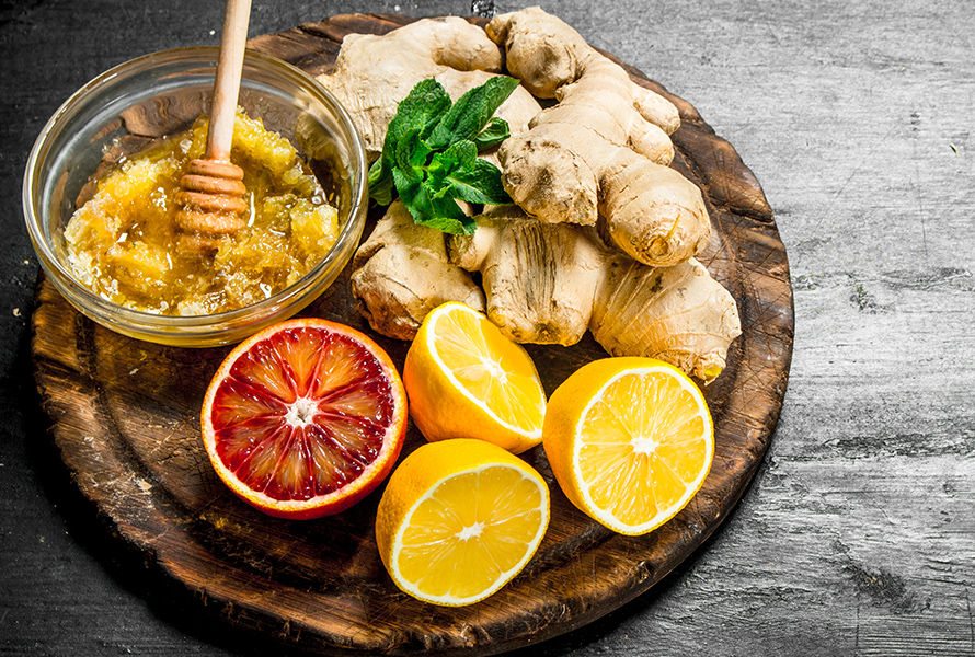 Auf einem Holzbrett liegen frischer Ingwer, Honig, Zitronen und eine Blutorange – bewährte Hausmittel gegen Schwangerschaftsübelkeit, voller Vitamine und Mineralstoffe.