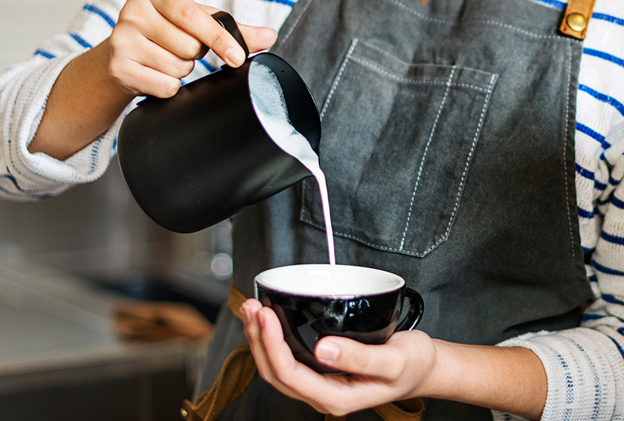 Barista bereitet Kaffee zu Eine Barista arbeitet konzentriert beim beim Eingiessen der Milch – kleine Genussmomente helfen beim Durchatmen im Alltag.