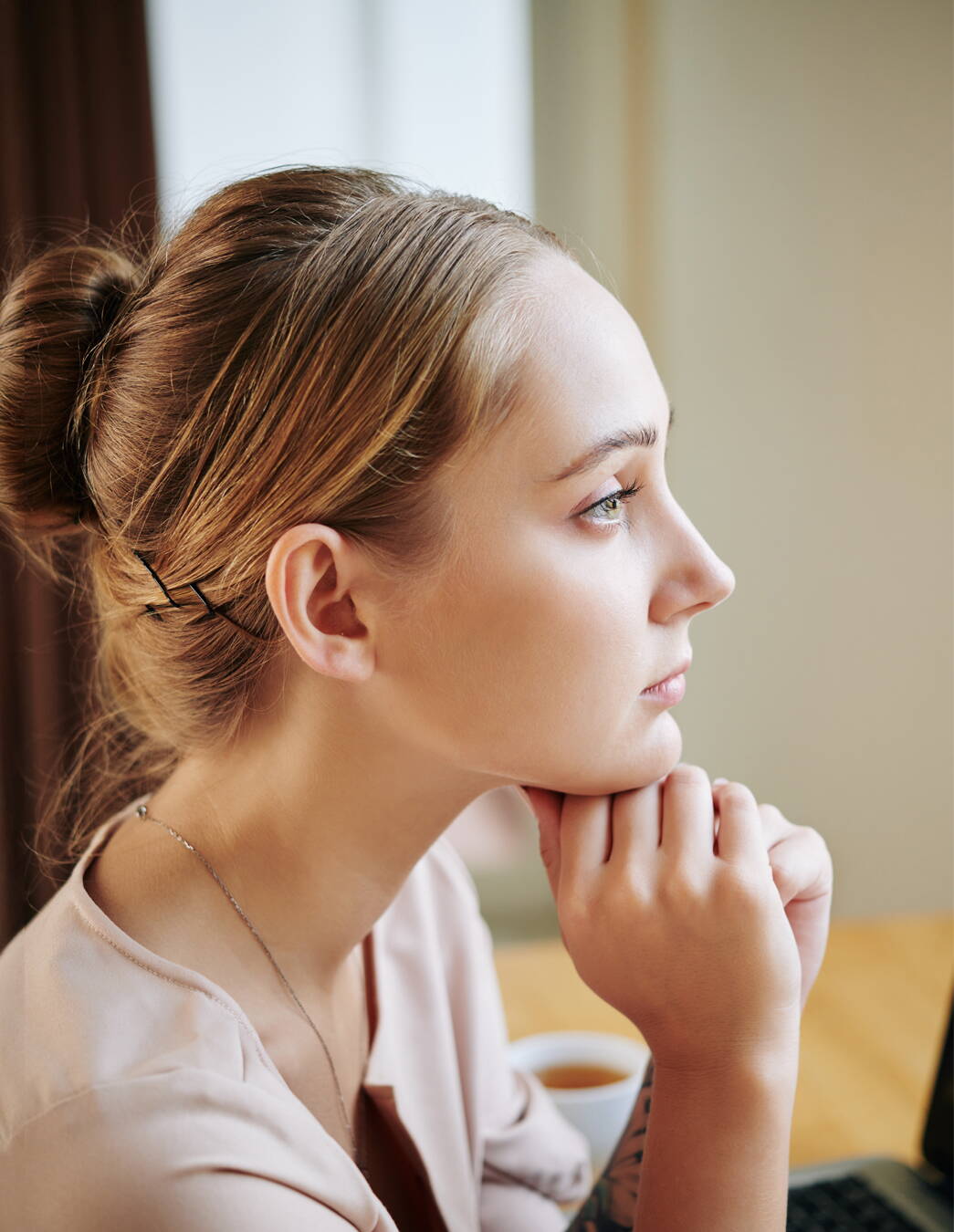 Une jeune femme de profil soutient son menton avec les mains et regarde dans le vide, perdue dans ses pensées – un moment typique de la démence de grossesse

