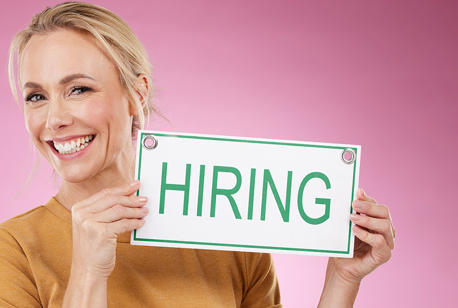 Sprigionare impatto – si candidi ora Una donna solleva un cartello con la scritta «Hiring» – lavorare in PRO LIFE significa: assumere compiti significativi ed essere parte di una comunità impegnata.
