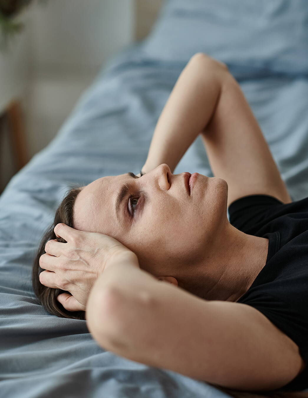 Eine hochschwangere Frau liegt unruhig im Bett, die Hände an den Kopf gelegt – typische Schlafprobleme in der Spätschwangerschaft.