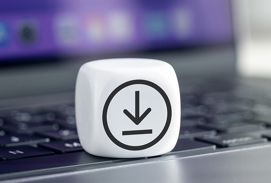 Das Bild zeigt einen weißen Würfel mit einem schwarzen Download-Symbol darauf, der auf einer Laptop-Tastatur platziert ist. Im Hintergrund ist ein unscharfer Bildschirm mit violetter Farbgebung zu sehen. Der Würfel symbolisiert den Bereich Downloads und hebt die Bedeutung des Herunterladens von Dateien in einer digitalen Umgebung hervor.