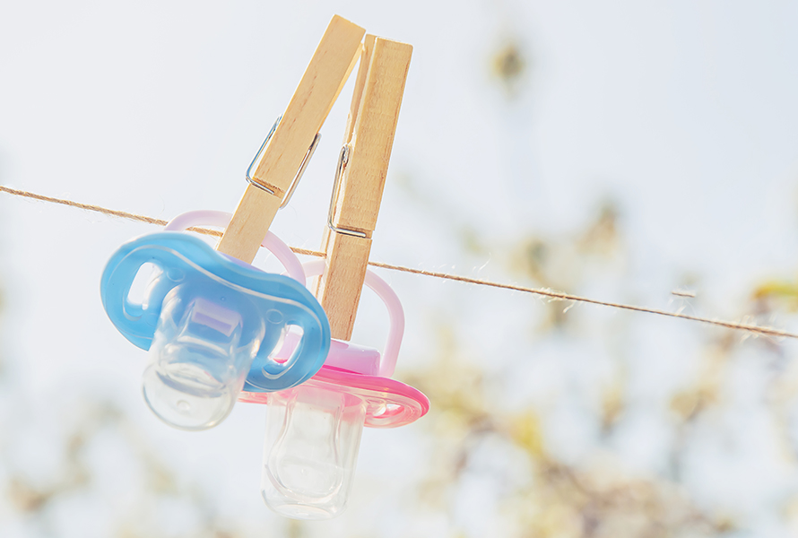 Rosa und hellblauer Nuggi an der Wäscheleine Zwei Nuggi (Schnuller) in klassischem Rosa und Hellblau hängen an einer Leine – Symbol für die Frage nach dem Geschlecht Ihres Babys.