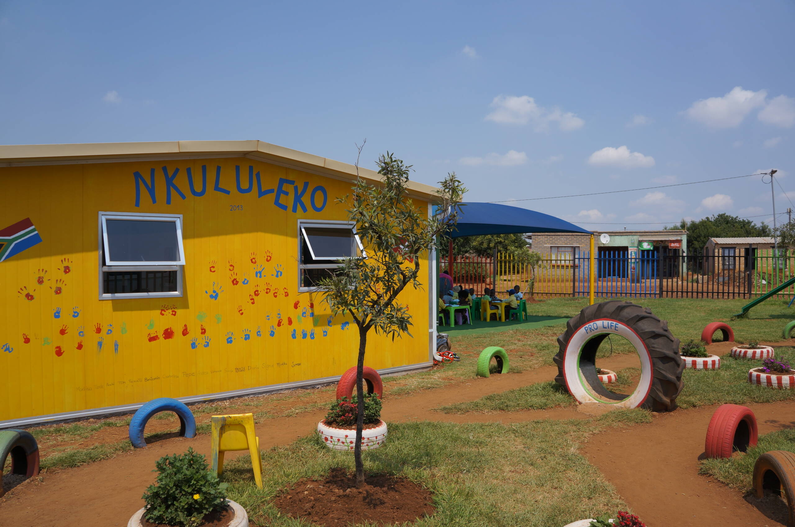 Ein Platz zum Spielen und Lernen Das neue Kita-Gebäude mit Spielplatz und Sonnenschirm – ein Ort, an dem Kinder geschützt spielen, lernen und sich entfalten können.