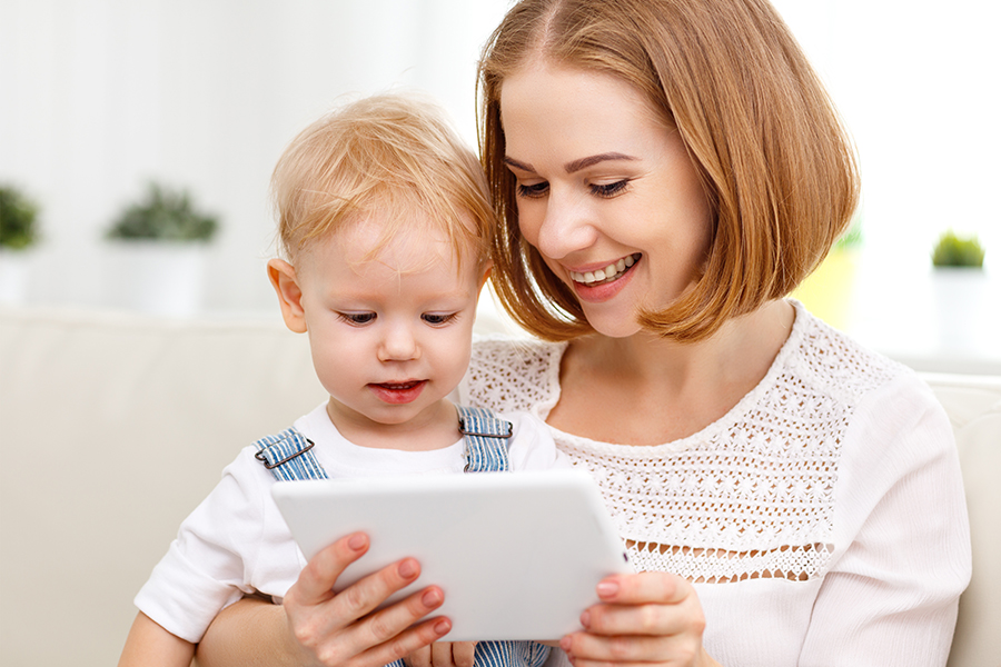 Eine junge Frau zeigt einem kleinen Jungen ein Tablet – ein Zeichen für Unterstützung, Bildung und digitale Nähe.