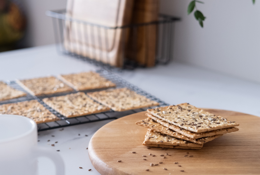 Knackiger Klassiker – Selbstgemachtes Knäckebrot Frisch gebackene Knäckebrotscheiben kühlen auf einem Gitter aus, im Vordergrund liegen einige Scheiben auf einem Holzbrett. Der ballaststoffreiche Snack für jede Tageszeit – pur oder belegt.
