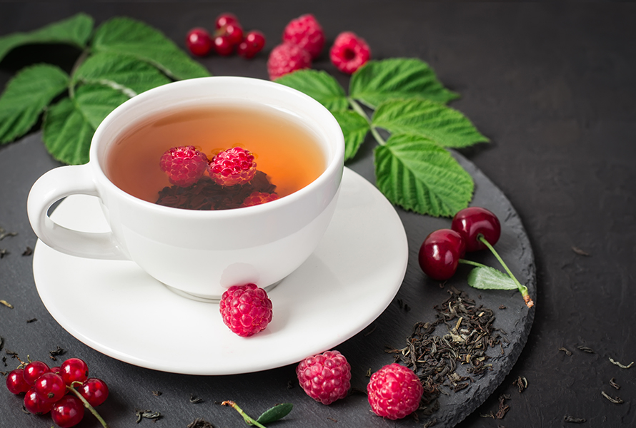 Himbeerblättertee zur Vorbereitung Eine Tasse Himbeerblättertee, umgeben von frischen und getrockneten Himbeerblättern sowie Himbeeren – ein bewährtes Hausmittel in den letzten Schwangerschaftswochen.