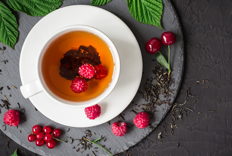 Himbeerblättertee – jetzt ist Pause Eine Tasse Himbeerblättertee zwischen frischen und getrockneten Himbeerblättern – in dieser Woche wird der Tee abgesetzt, doch im Wochenbett kann er weiterhin hilfreich sein.
