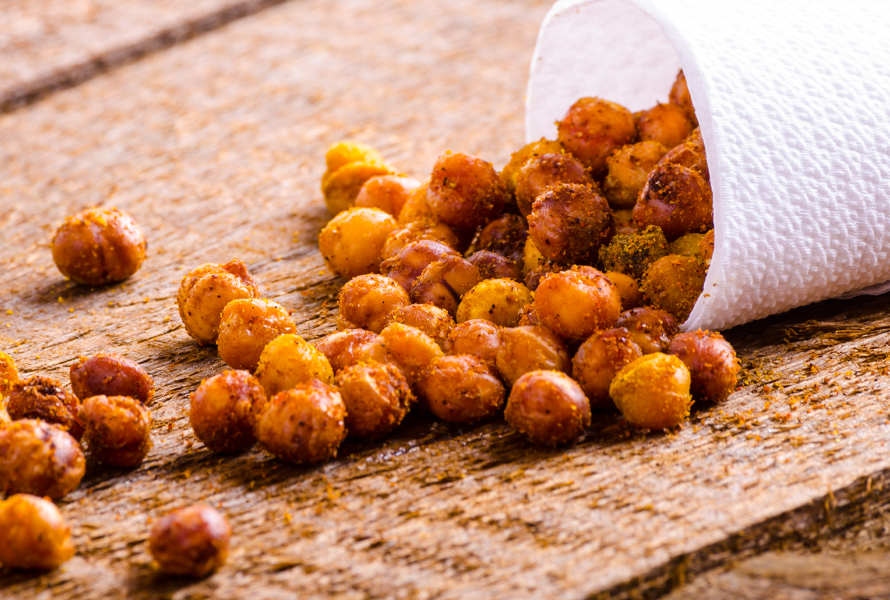 Knusprig und würzig – Geröstete Kichererbsen Goldbraune Kichererbsen rollen aus einer geöffneten Papiertüte auf einen rustikalen Holztisch. Ein gesunder, ballaststoffreicher Snack – knusprig, aromatisch und einfach selbst gemacht.