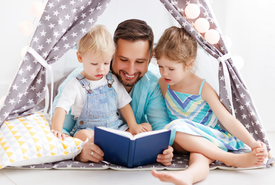 Abenteuer Wohnzimmer Ein Vater liest seinen Kindern im selbstgebauten Wohnzimmerzelt vor – ein Moment voller Geborgenheit, wie ihn PRO LIFE im Alltag möglich macht.