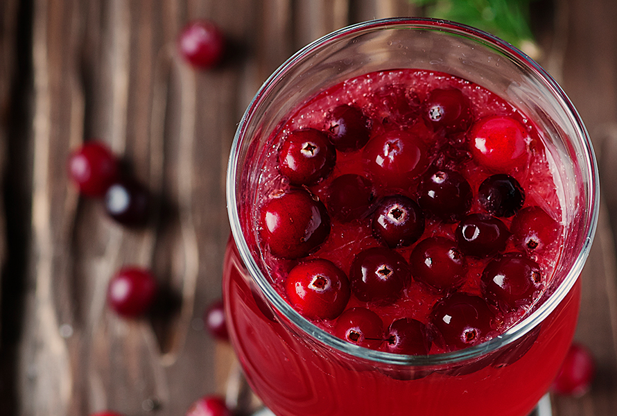 Ein Glas leuchtend roter Cranberrysaft mit frischen Cranberrys – unterstützend bei beginnender Blasenentzündung und als mildes Hausmittel in der späten Schwangerschaft.