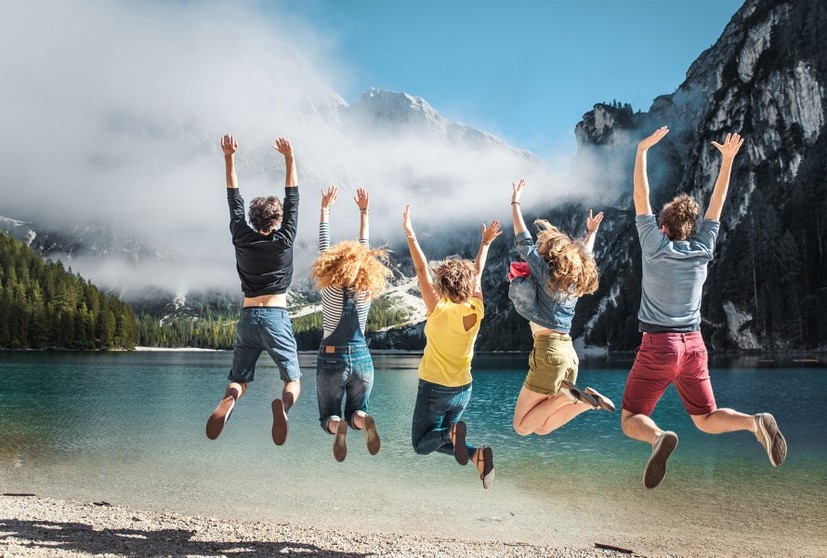 Vivre plus – avec MiBon Le même groupe de jeunes saute en l’air – avec vue sur le lac et les montagnes. La joie de vivre pure rendue accessible grâce à MiBon.