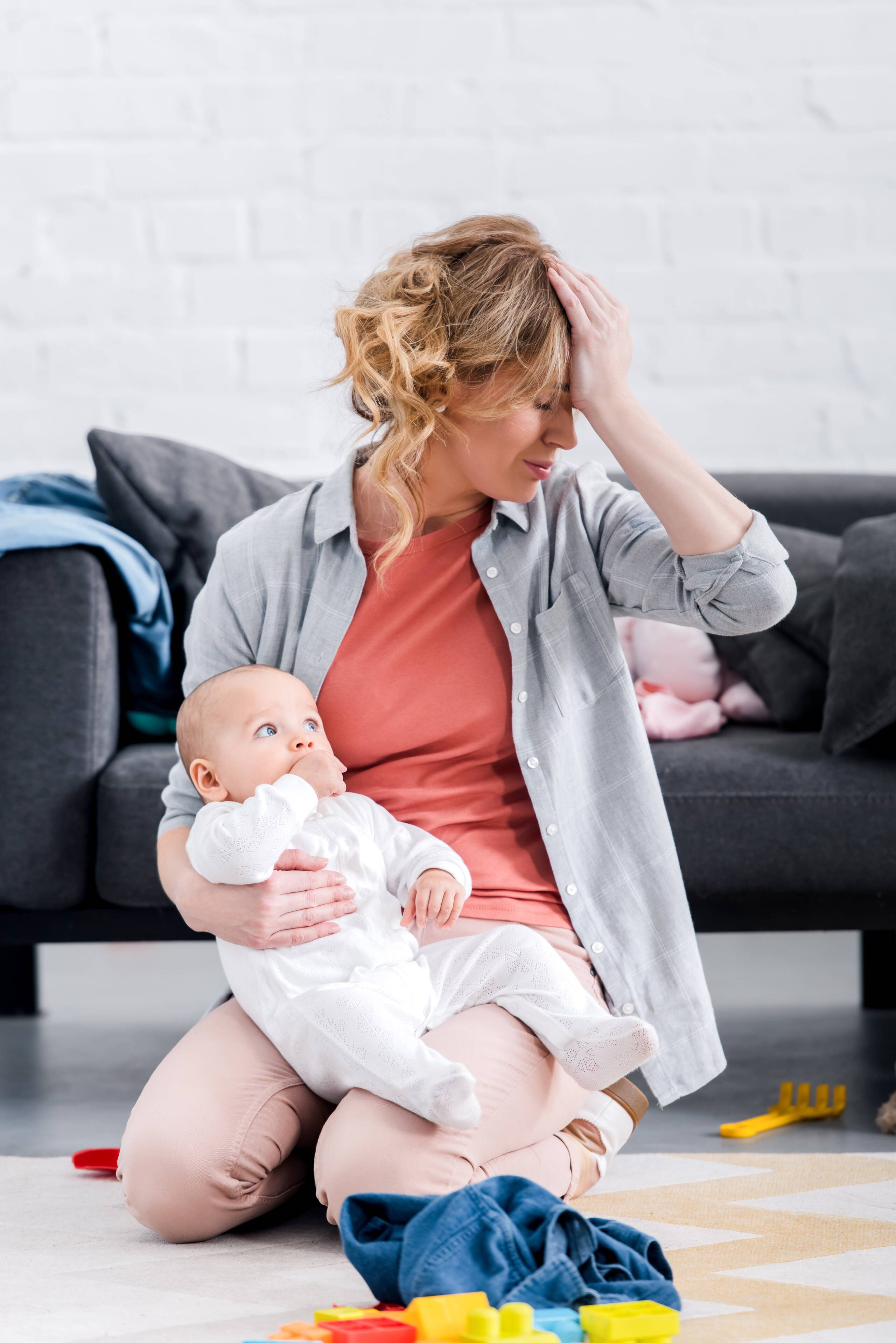 Sovraccarico nella vita quotidiana – Madre con bambino L’immagine mostra una madre seduta a terra con il suo bambino, circondata da giocattoli e oggetti quotidiani. Rappresenta una situazione di sovraccarico e la necessità di sostegno nella vita familiare.