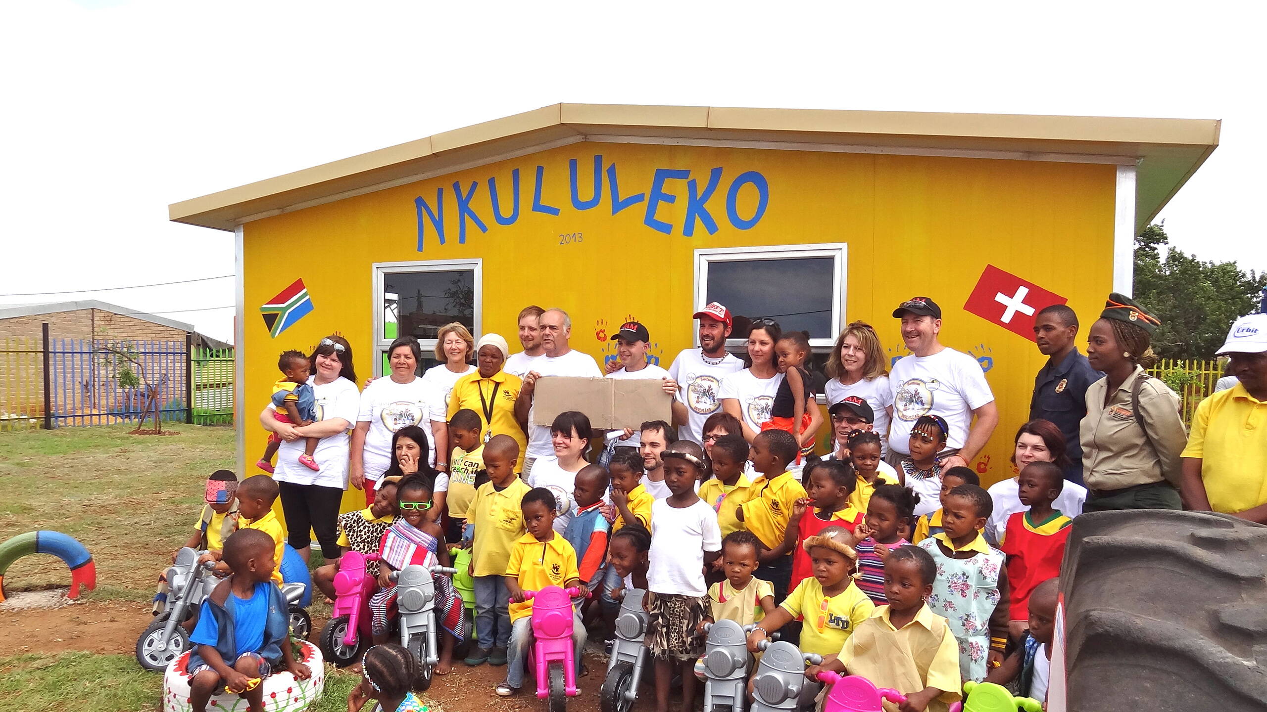 Das Bauteam von PRO LIFE steht stolz vor dem Neubau der KITA Nkululeko. Davor: lachende Kinder, die den neuen Ort für Bildung und Geborgenheit begeistert einweihen.









