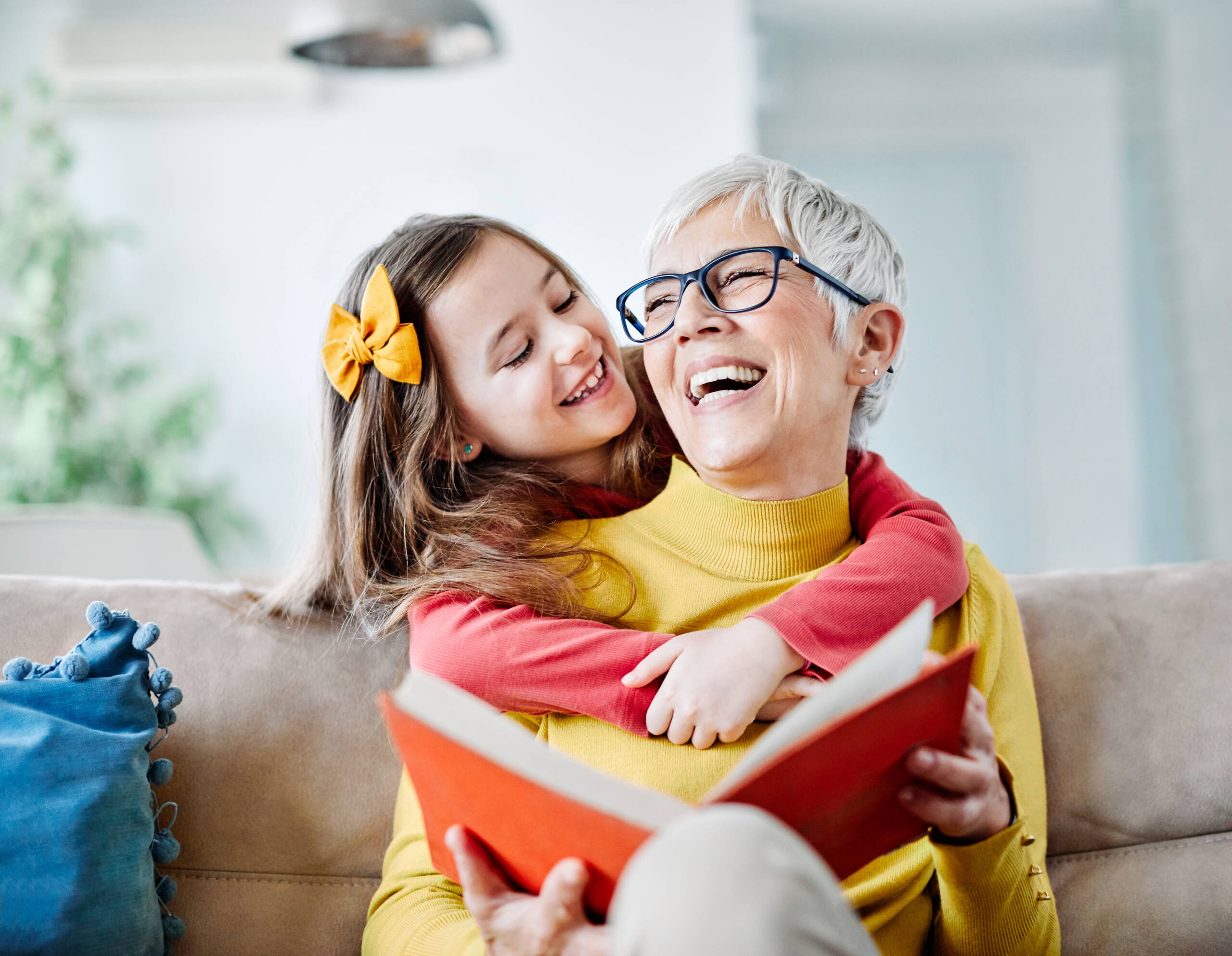 Supporto quotidiano – Solidarietà tra generazioni Una persona anziana è seduta su un divano con un libro, accompagnata da una persona più giovane. L’immagine rappresenta la cura, la vicinanza umana e il sostegno pratico nella vita quotidiana.