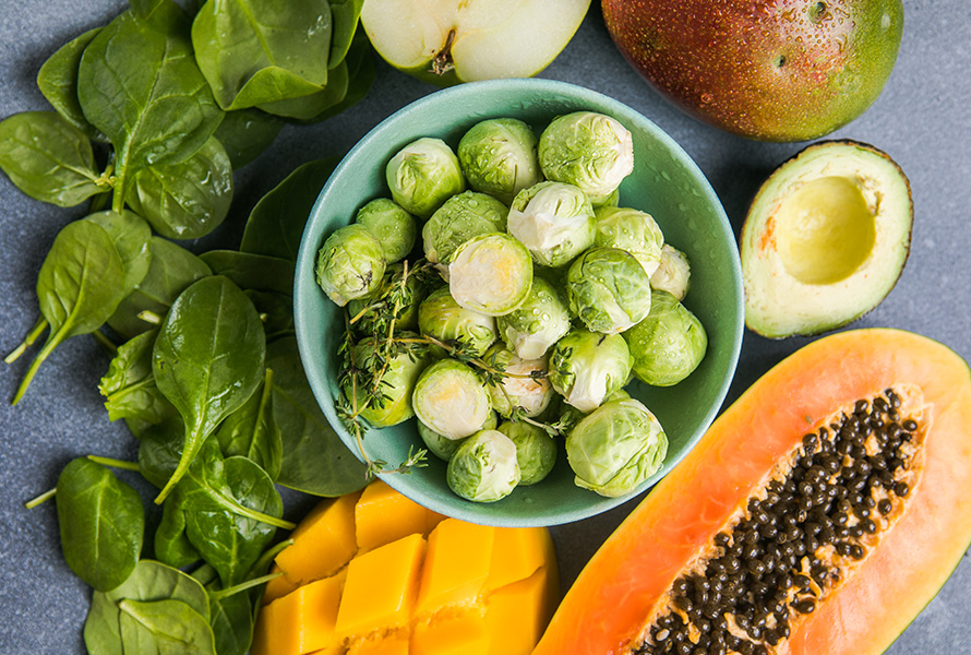 Natürliches Folat für die Entwicklung Eine Auswahl an folatreichen Lebensmitteln: Rosenkohl, Papaya, Mango, Spinat und Apfel – ideale Begleiter in der Schwangerschaft.