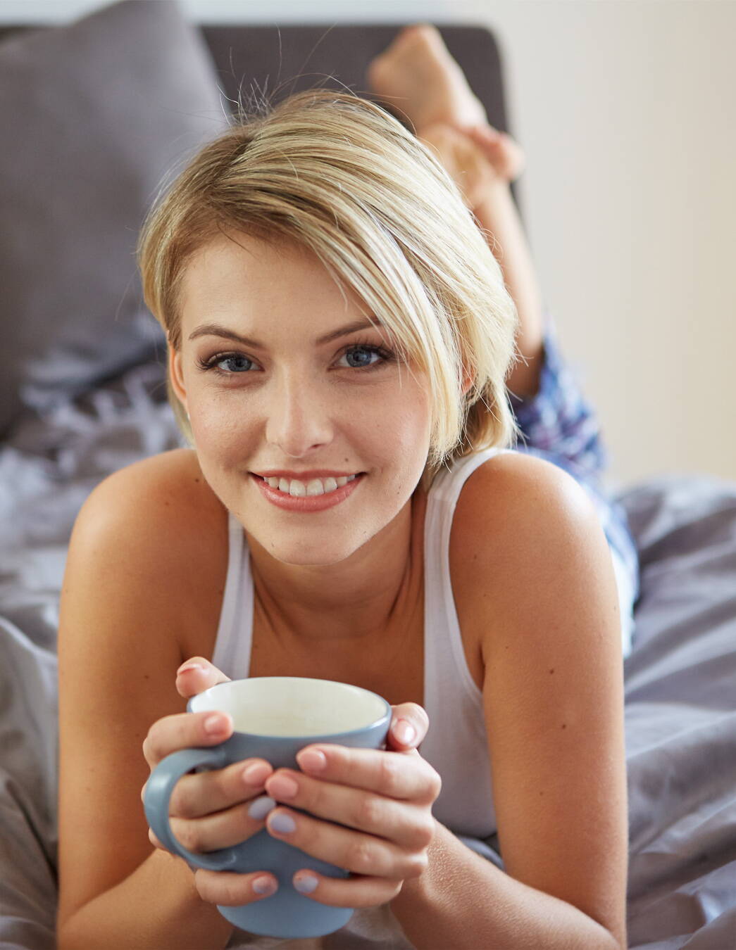 Jeune femme allongée sur le ventre, détendue, tenant une tasse de tisane d’allaitement – symbole de calme et de soutien à la lactation après l’accouchement.