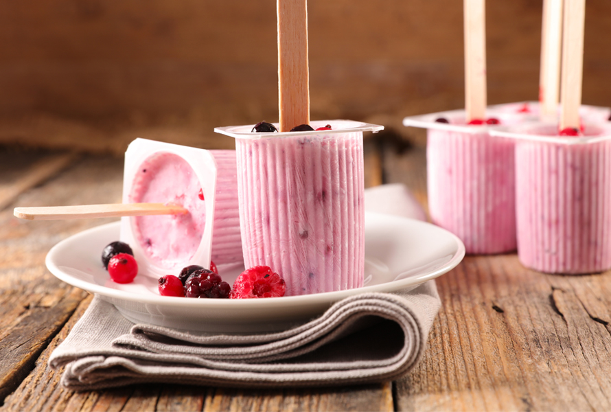 Piccoli bicchieri di yogurt con gelato allo yogurt fatto in casa e frutti di bosco freschi, su un piatto bianco con tovagliolo beige – un piacere leggero e ricco di proteine.

