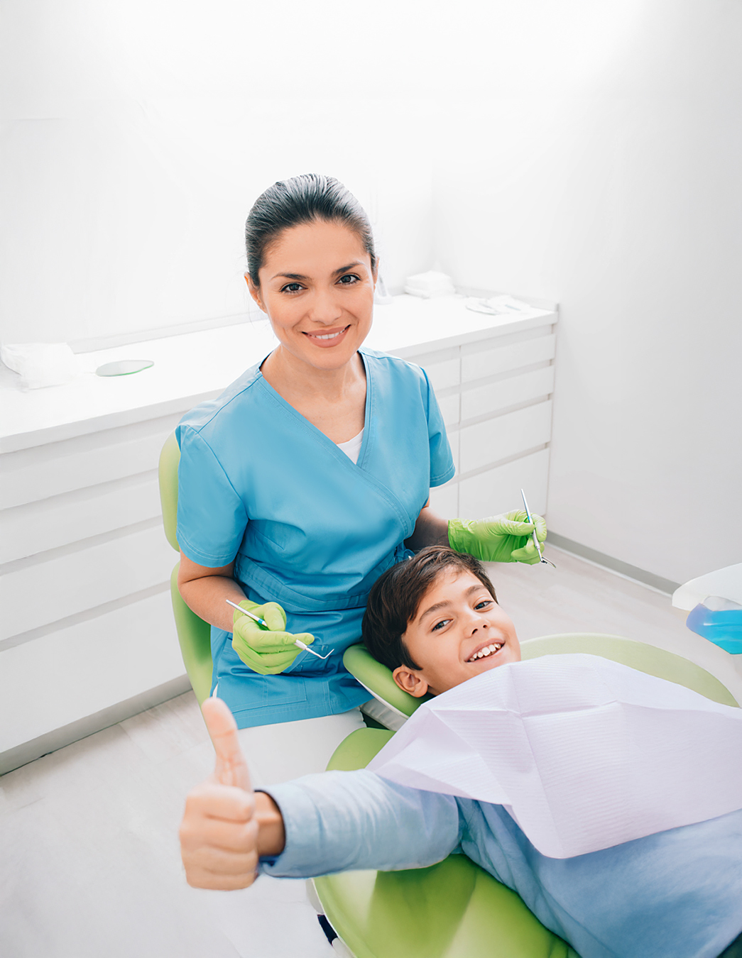 Prevenzione dentale con un sorriso Una giovane dentista cura un paziente, mentre un ragazzo sorride alla fotocamera con il pollice alzato – un forte segno di fiducia e buona assistenza.