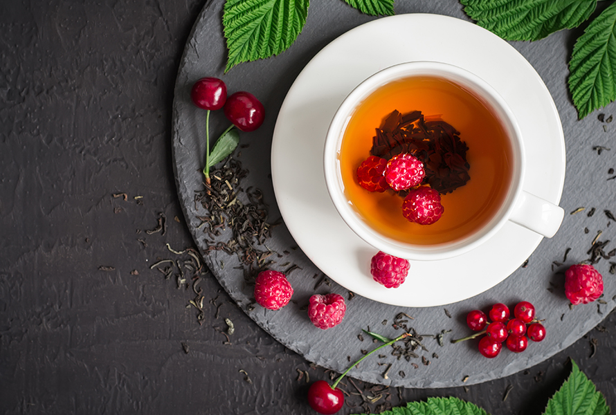 Trinkpause beim Himbeerblättertee Eine Tasse Himbeerblättertee, dekorativ umgeben von frischen und getrockneten Himbeerblättern sowie Himbeeren – diese Woche ist eine Einnahmepause angesagt.