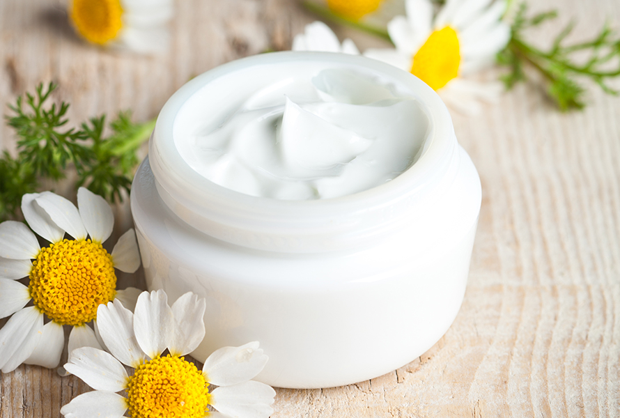 Selbstgemachte Handcreme mit Kamille Ein Tiegel mit cremiger Kamille-Handpflege, umgeben von frischen Kamillenblüten – sanfte Pflege für empfindliche Haut in der Schwangerschaft.