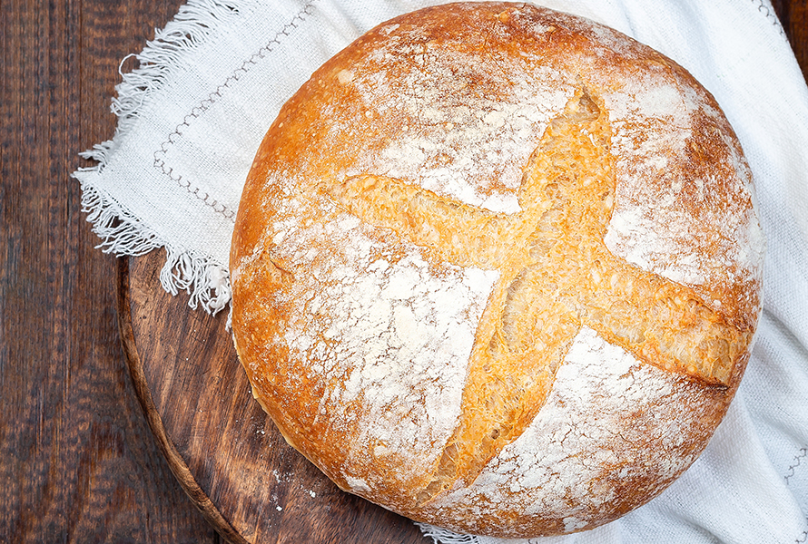Frisch gebackenes rundes Brot Ein selbstgebackenes Brot liegt auf einem Holzbrett – gesünder und sättigender als industrielles Brot.