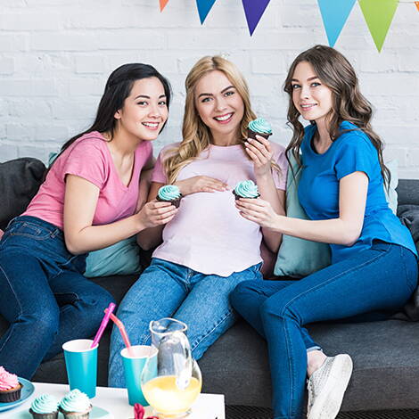 Gemeinsam feiern vor der Geburt Eine Schwangere sitzt mit zwei Freundinnen auf dem Sofa – Babyparty-Stimmung mit Snacks, Gesprächen und kleinen Spielen.