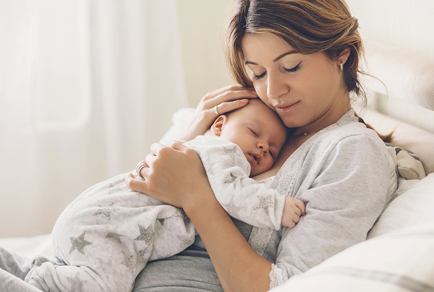 Mutter mit schlafendem Baby auf dem Bauch Eine Mutter hält ihr Baby zärtlich auf dem Bauch, eine innige Szene, die Geborgenheit und Nähe zeigt.