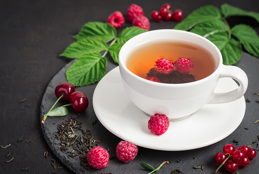 Eine Tasse mit Himbeerblättertee, frischen und getrockneten Blättern sowie Himbeeren – ein natürlicher Begleiter zur Geburtsvorbereitung.
