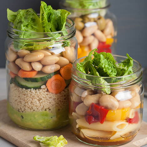 Salat im Glas – bunt, praktisch, gesund Drei Gläser gefüllt mit geschichtetem Salat aus Couscous, Pasta, Gemüse, Bohnen, Oliven und Blattsalat – ideal für unterwegs oder als Vorrat.