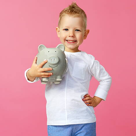 Dono del cuore – Insieme per aiutare Un bambino tiene un salvadanaio grigio davanti a uno sfondo rosa. L’immagine simboleggia il conto donazioni del Dono del cuore e trasmette l’idea di solidarietà e sostegno.