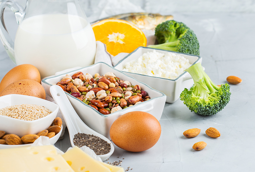 Auswahl magnesiumreicher und kalziumhaltiger Lebensmittel wie Hülsenfrüchte, Hüttenkäse, Milch, Eier, Broccoli, Chiasamen und Käse für eine ausgewogene Ernährung.