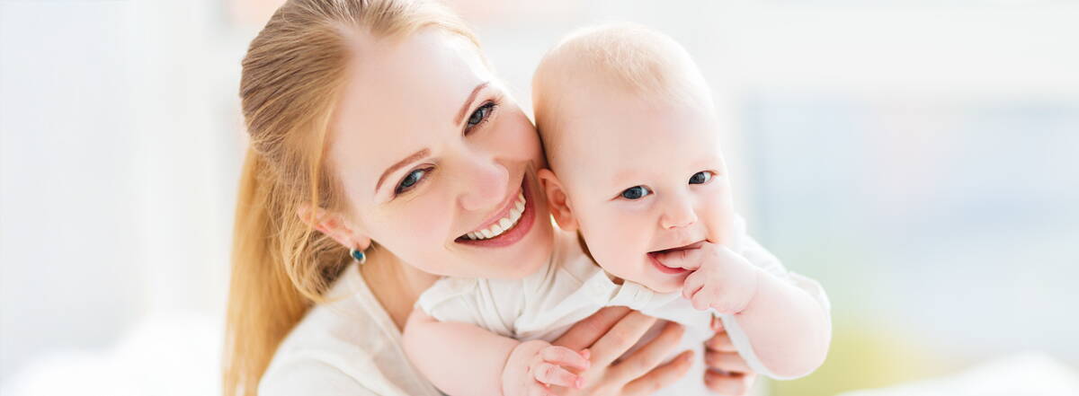 Assicurato in modo familiare Una madre tiene amorevolmente in braccio il suo bambino piccolo. Entrambi ridono – un momento che mostra quanto sia importante la sicurezza per tutta la famiglia.