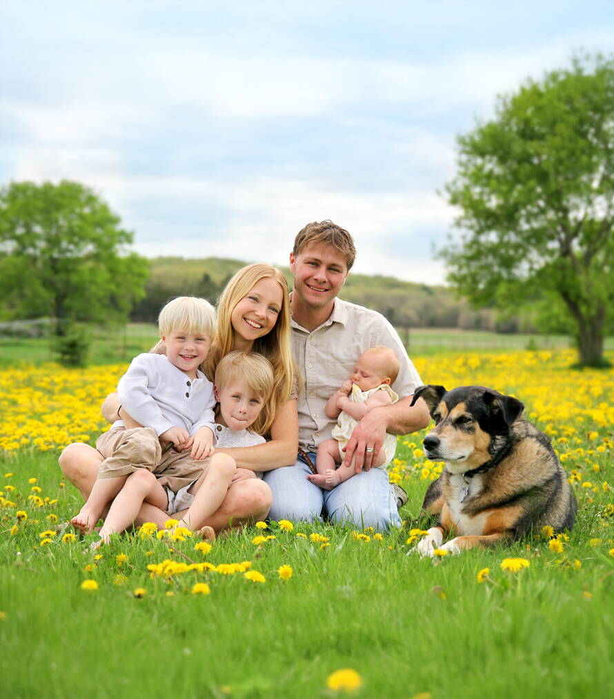 Un printemps plein de vie Une jeune famille avec trois enfants et un chien est assise joyeusement dans un pré fleuri – symbole de renouveau, de joie de vivre et de solidarité.
