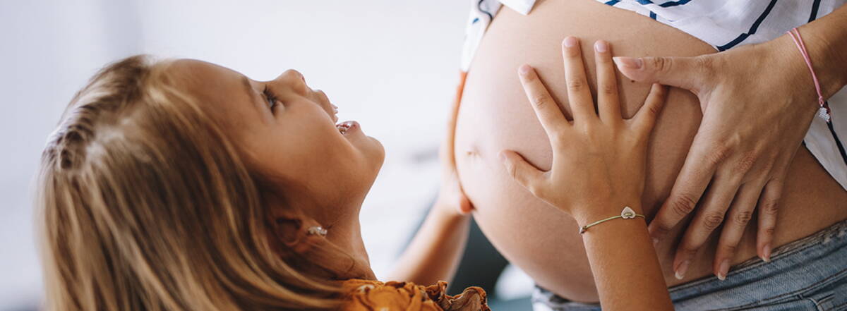 Blog gravidanza e bebè Una bambina posa le mani sulla pancia di una donna incinta – uno sguardo affettuoso verso un futuro condiviso.